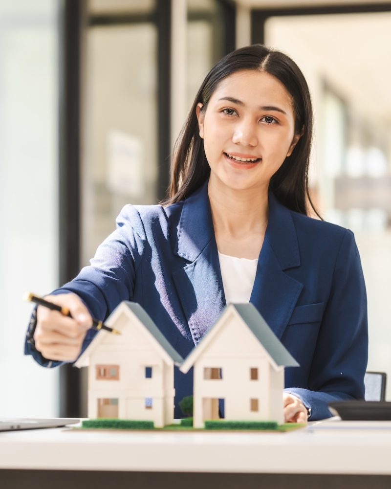 Attractive Asian real estate agent in a formal suit presents a model home to clients
