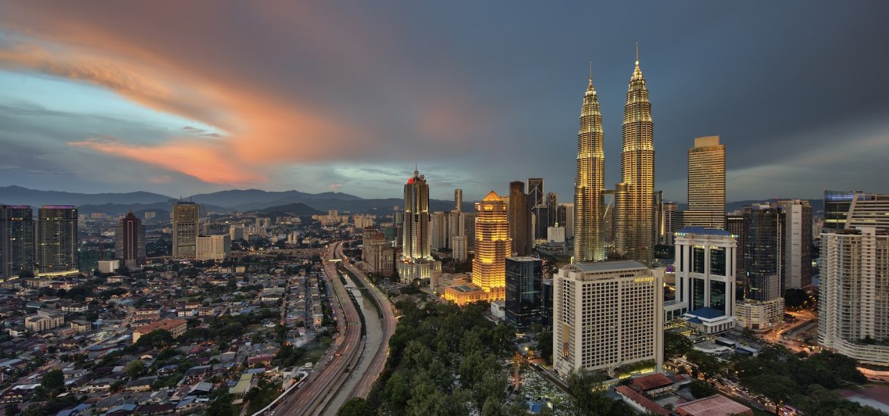 Cityscape of Kuala Lumpur, Malaysia at dusk, with illuminated Petronas Towers in the distance.