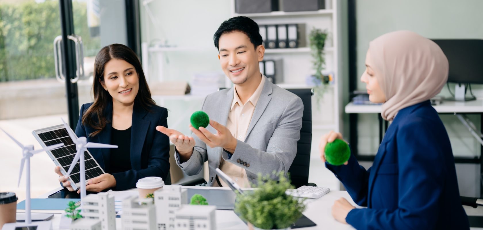 Group of diverse multiethnic businesspeople standing neare table looking at model of building from residential project. Green business company and Solar Energy Environment city Concept.