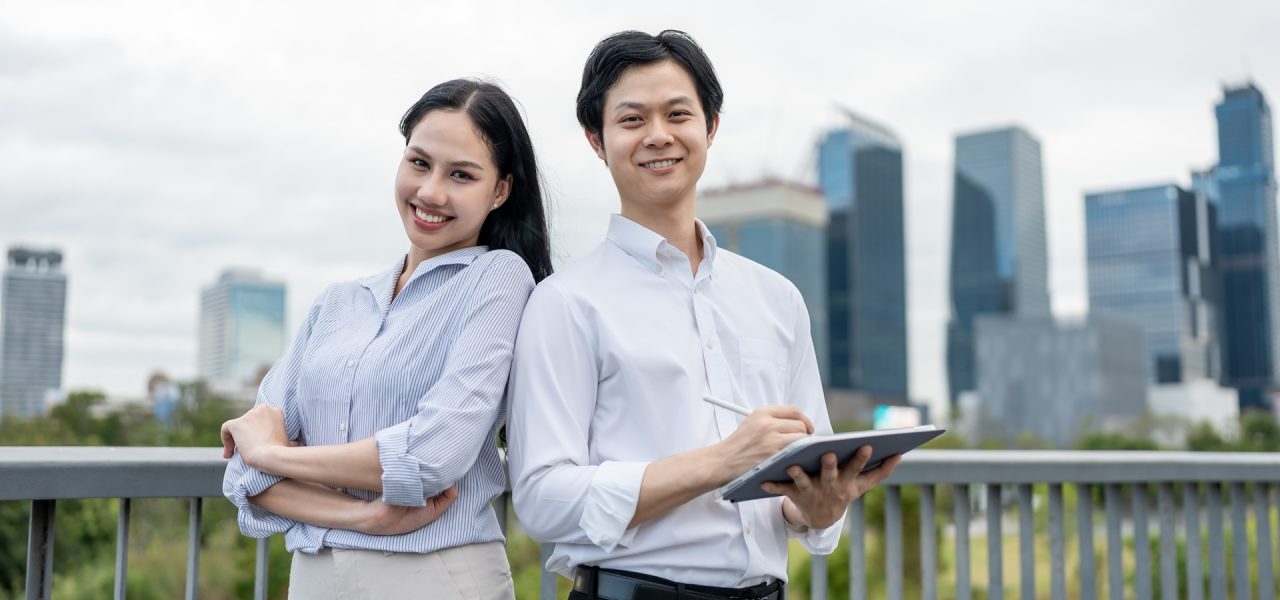 Portrait of Asian young businessman and woman partner standing in city. Attractive colleagues employee people feel happy and relax while spending time outside office company together with confidence.