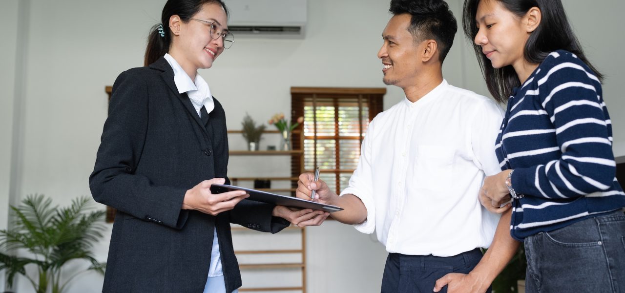 Young happy smiling couple read agreement with realtor and looking through the contract of real estate sale going to signing a deal.